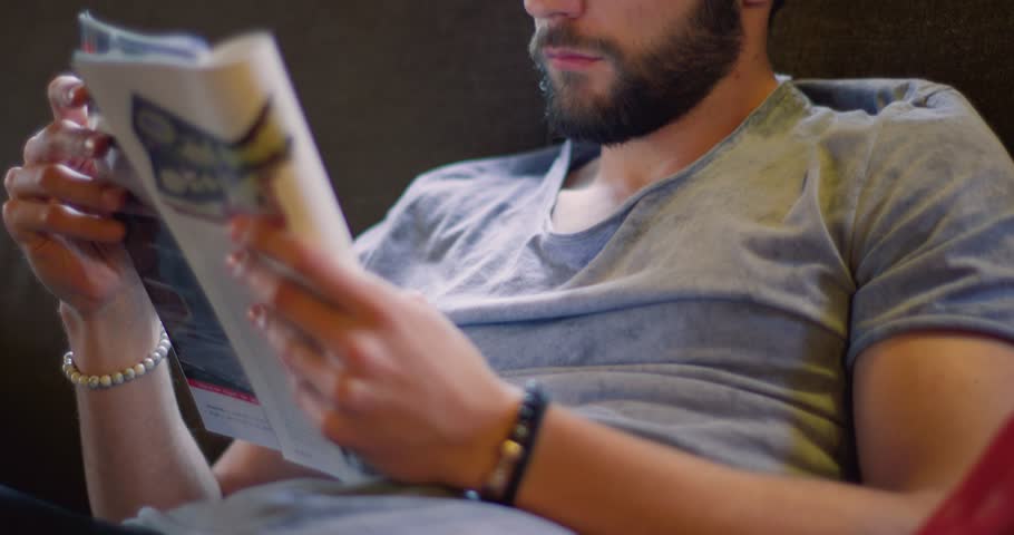 Youg millennial man relaxing reading magazine newspaper at home in casual dressing. 4k video