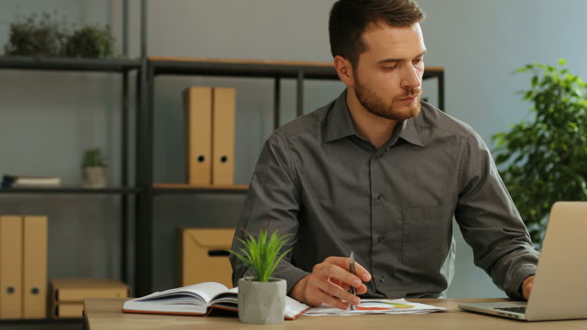 Handsome young business man working on laptop computer in the office and analizing the diagrams fron the finance report.