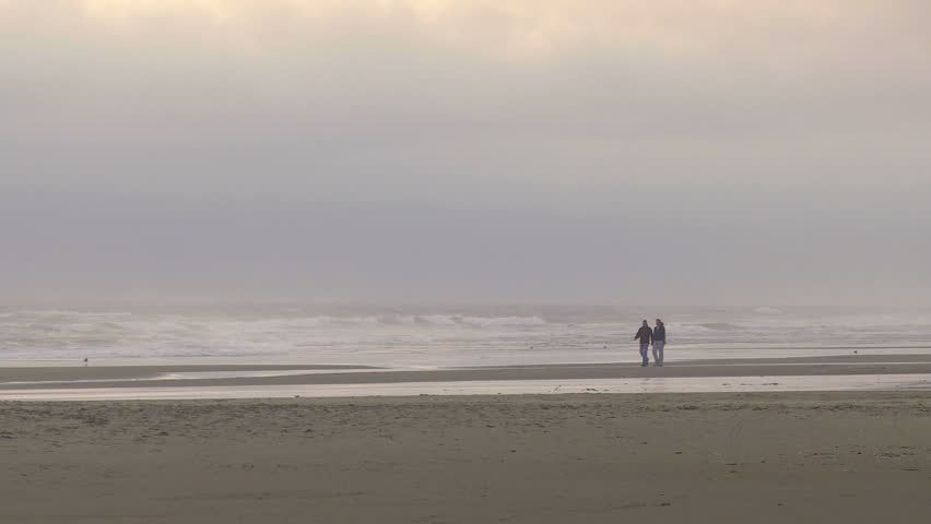 Couple walking on windy evening beach in Oregon, USA