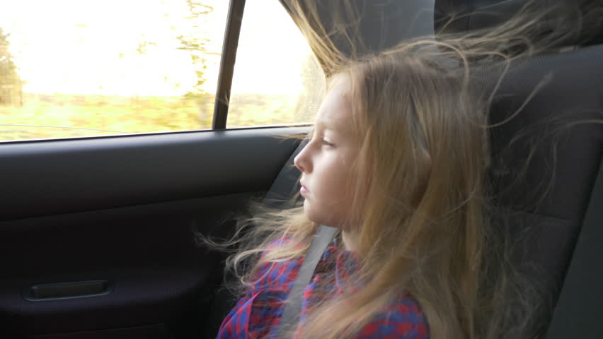Young beautiful girl on adventure road trip inside car the wind in her hair. Pretty serious white girl. Road speed drive strong wind. Travel autumn sunset. Backlit light sunbeam.