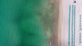Aerial tropical static beach video footage with vertical coastline showing turquoise green clean beach waves breaking against white sandy background with blue umbrella and tourists splashing in water 