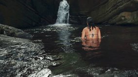 A woman swimming and relaxing inside river by waterfall