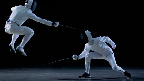 Two Professional Fencers Show Masterful Swordsmanship in their Foil Fight. They Dodge, Leap and Thrust and Lunge. Shot Isolated on Black Background and in Slow Motion. 4K UHD.