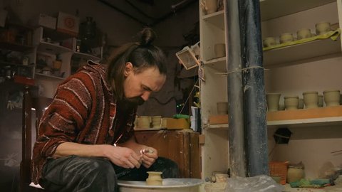 Professional male potter shaping mug with special tool in pottery workshop, studio. Crafting, artwork and handmade concept