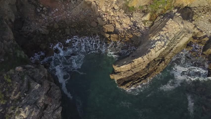 Drone footage over beach with crashing waves rocks