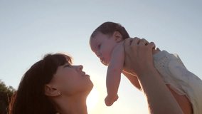 Mother is playing with small child in her arms and against blue sky