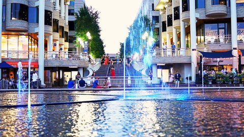 Washington DC, USA - August 4, 2017: Ground level closeup view of colorful fountain at night in Georgetown Harbor with restaurants and people walking at waterfront park