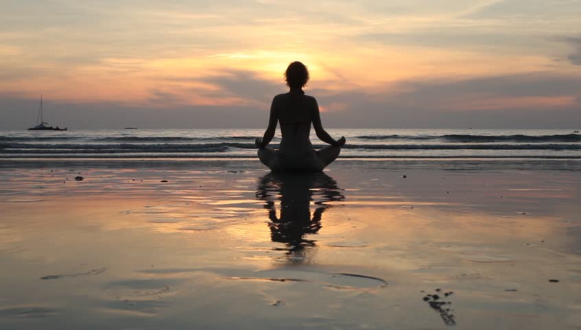 Young yoga woman meditating in lotus pose on the beach at sunset 