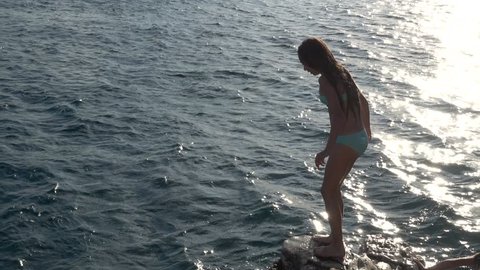 Little beautiful girl jumping from stone to sea on Adriatic coast of Croatia.
