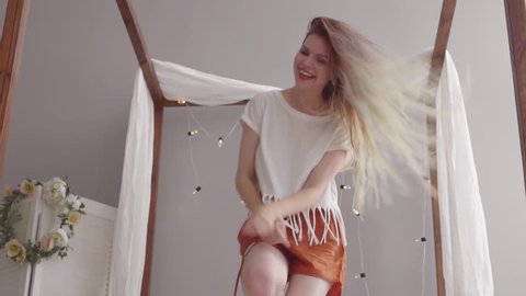 Happy young blonde female whith pretty long hair in pajama jumping and dancing on bed in morning and smiling. Woman in cheerful mood. Slow mo .