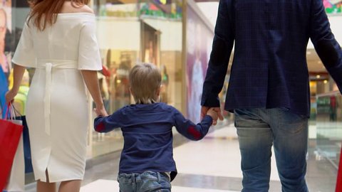 The boy holds a hand from the mother and the father. Parents not Sousse packages with Christmas gifts. Family Christmas shopping. The boy with parents go along the corridor shopping center. Christmas