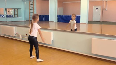 A beautiful girl is engaged in dancing in the dance hall. The child looks at the reflection and performs the exercises. Dancing school.