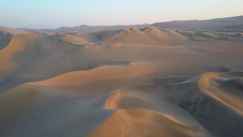 Aerial drone footage on a sunny day above sand dunes of Peru. Close to Ica and Huacachina. Similar to Sahara and Emirates Deserts. Boogie cars driving and people sandboarding. Color Corrected.