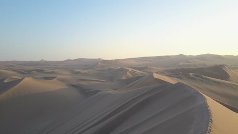 Aerial drone footage on a sunny day above sand dunes of Peru. Close to Ica and Huacachina. Similar to Sahara and Emirates Deserts. Boogie cars driving and people sandboarding. Oasis nearby.