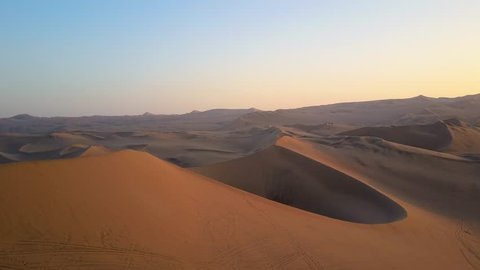 Aerial drone footage on a sunny day above sand dunes of Peru. Close to Ica and Huacachina. Similar to Sahara and Emirates Deserts. Boogie cars driving and people sandboarding. Color Corrected.