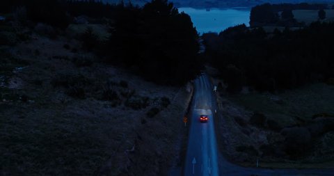 Aerial view car driving on country road at dusk through dark forest with headlights