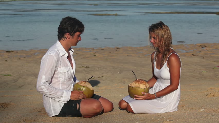 Attractive couple drinking coconuts and sitting on beach