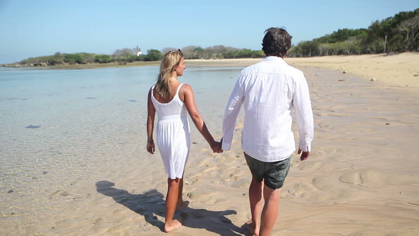 Rear view of couple holding by hands and walking along coastline