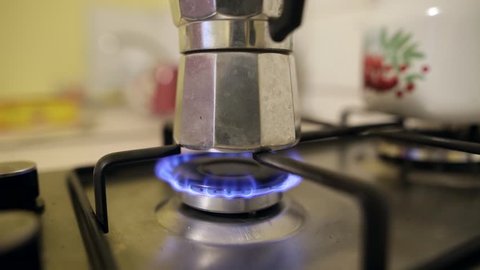 Moka pot coffee maker on a gas cooking hob. lose-up of an Italian coffee maker on a stove. Unrecognizable person washes his hands in the background. Static shot.