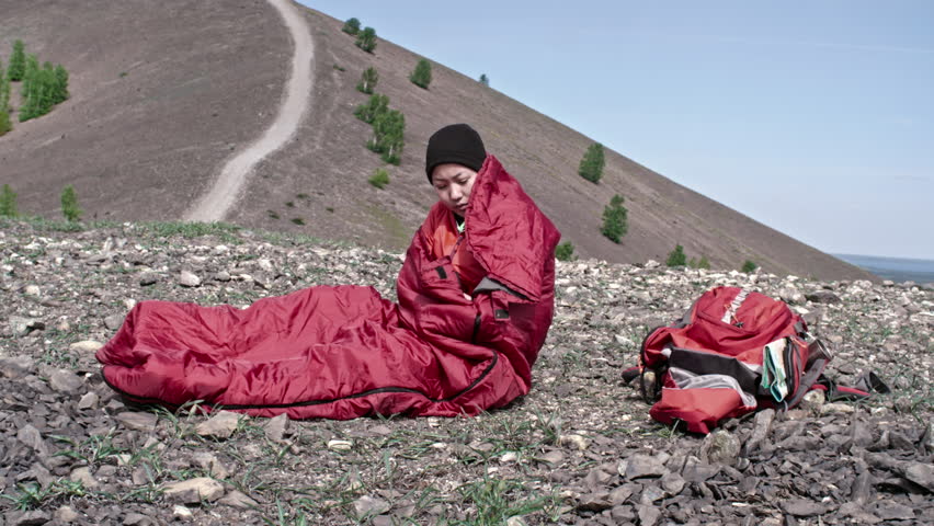 Asian woman solo hiker falling asleep in her sleeping bag while camping in mountains