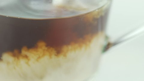 Milk and coffee. Cappuccino. Great macro slow-motion shot of pouring fresh milk into a glass transparent mug with coffee or tea inside of it. Slow motion in a white background.