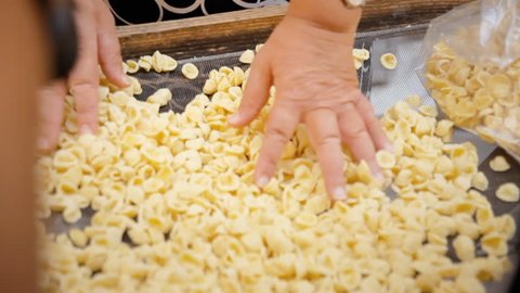 A woman touching orecchiette pasta drying on a board at an Italian street market.
