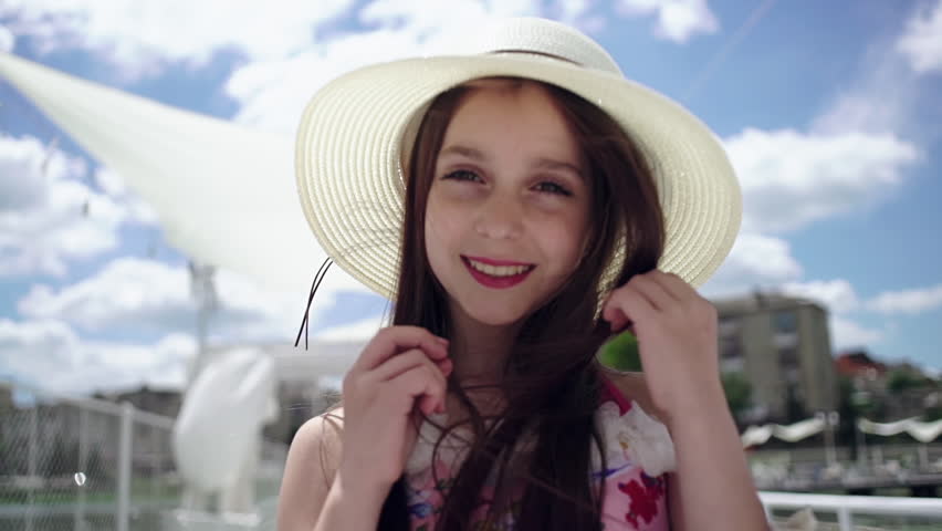 Young little girl at the pier with a beautiful bonnet and a bright swimsuit. Summer holiday at the pier.