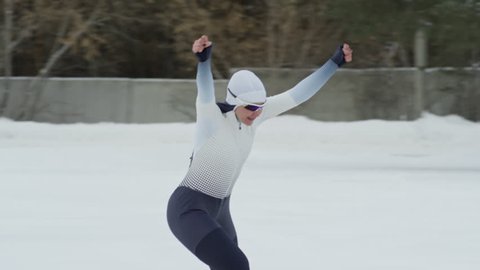 Tracking with slowmo of female speed skater raising her arms and celebrating after winning race against teammate during practice in outdoor ice rink in winter