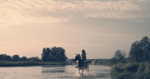 Slow motion shot. Woman wearing cowboy outfit riding horse on the background of beautiful sunset and water. Girl model on horseback on river water at sunset, backlit with sunshine.
