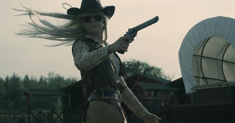 Country side female shooter in cowboy outfit. A girl with long hair, wearing cowboy's hat, holding gun, turning around to get ready to shoot