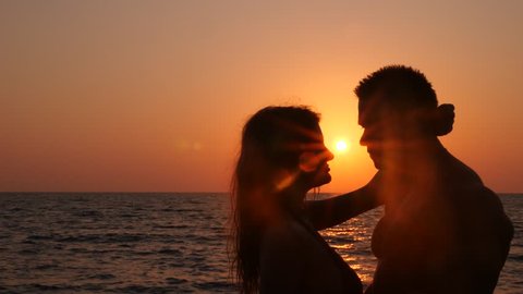 Silhouettes of pregnant women in bikini and romantic muscular man. the bodybuilder hugs, kisses his wife and strokes her belly. against the background of a sea sunset. 4k. Slow motion