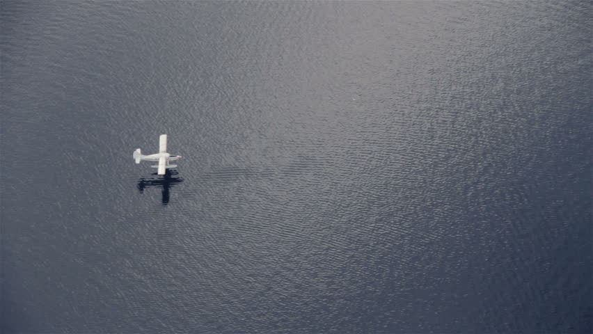 View from airplane of float plane on lake water approaching and landing