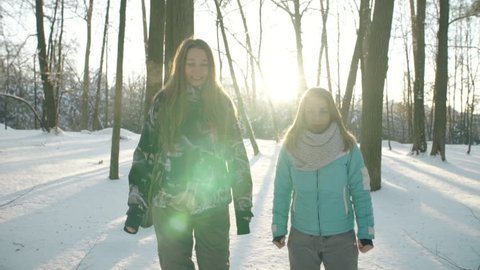 Two young women are running in the winter forest. Sunset in the snowy forest. The rays of the sun will fall into the frame. Two young women are enjoying of running, running on the camera.