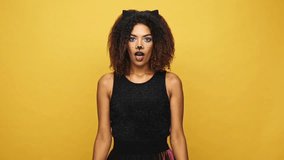 Pretty young afro american lady in cat costume and with make up surprising isolated over yellow