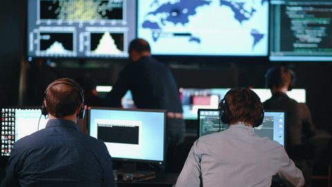 A team of security personnel working in a busy system control room, could be a weather station airport traffic control. It could be a power station or police army control facility.