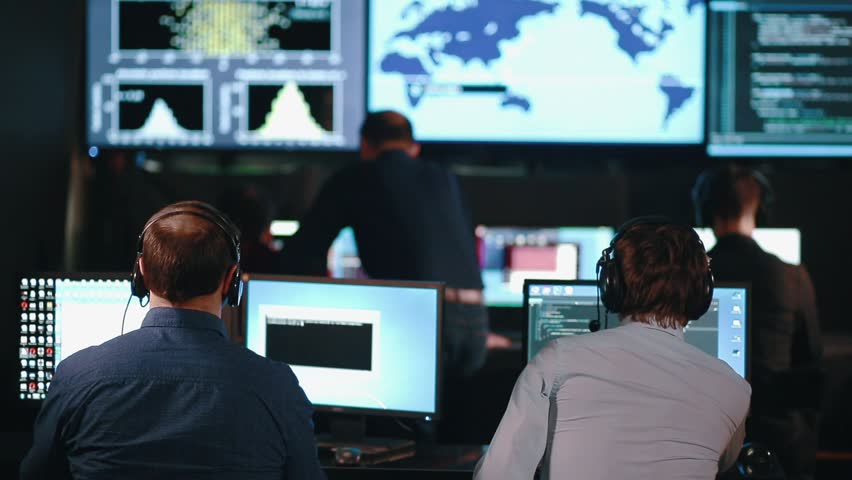 A team of security personnel working in a busy system control room, could be a weather station airport traffic control. It could be a power station or police army control facility. Royalty-Free Stock Footage #30940453