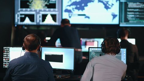 A team of security personnel working in a busy system control room, could be a weather station airport traffic control. It could be a power station or police army control facility.