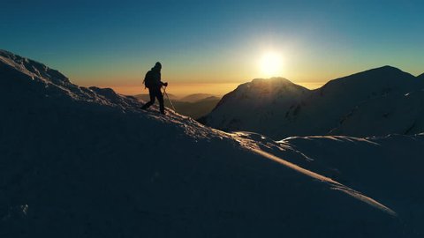 Aerial, slow motion - Close up shot of male mountaineer walking down the snowy mountain at sunset, edited version Arkistovideo