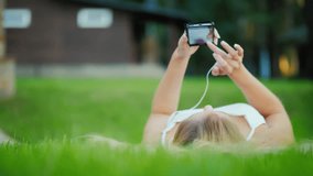 A young girl is lying on her back on the lawn, enjoying a smartphone. Video with shallow depth of field, low angle shooting from above