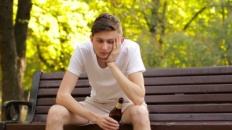 A drunk hipster sitting on a bench and drinking beer. Nausea and wobbling