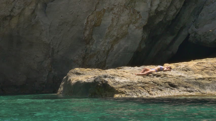Young woman sunbathing on a rock in the sea near a cliff in Ponza Island Italy