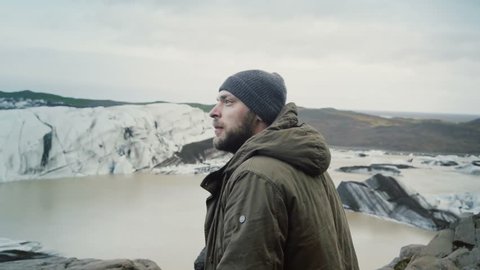 Young traveling man standing on the top of the mountain and looking on glaciers in Vatnajokull ice lagoon in Iceland.: film stockowy