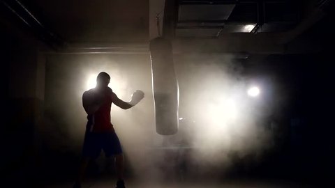 alone large boxer is working out blows on a punching bag in a dark gym