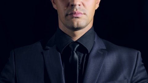 closeup of a man in black clothes on black background. 4k. Slow motion. man strokes his chin and looks at the camera. decision-making gesture