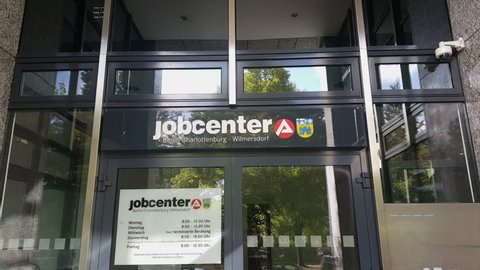 GERMANY - CIRCA SEPTEMBER 2017 - People exit jobcenter Wilmersdorf-Chalottenburg, doors, opening hours sign
