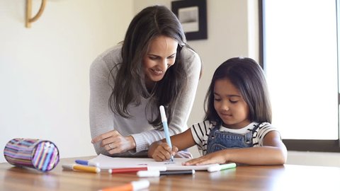 Happy mother and smiling daughter together painting using markers. Mother helping adopted child with art homework. Cheerful mother and asian little girl making painting at home.