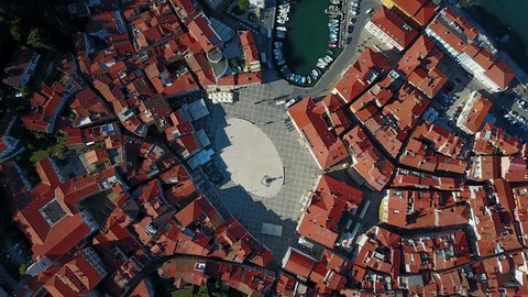 Flight over old city Piran in the morning, aerial top view with Tartini Square, St. George's Parish Church, marina and old roofs of the old houses. 
