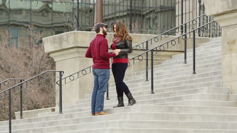 Man proposing on one knee to a woman on the steps of a building.