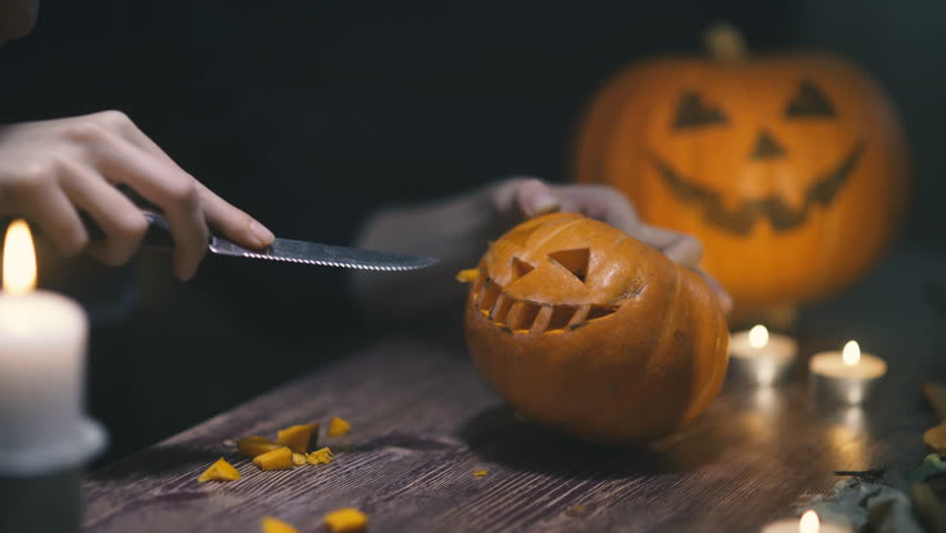 a woman hands cuts out a jack lantern smile with knife and removes seeds from a Halloween pumpkin with a wooden spoon. on a wooden table with kandle. halloween concetp.
