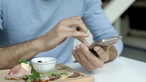 Man in blue sweater browsing internet on smartphone during lunch
